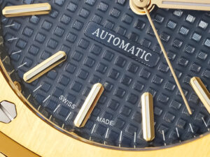 Close-up of the Royal Oak Yellow Gold watch with blue "Tapisserie" dial, gold hour markers, and "Automatic" text detail.