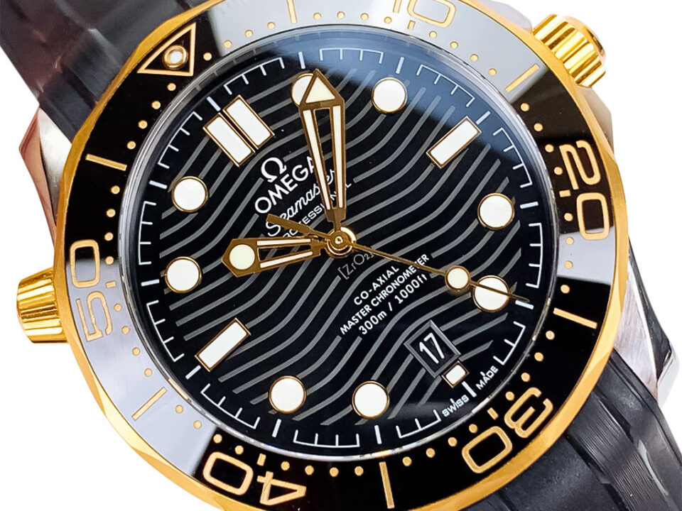 Seamaster Diver 300 watch in stainless steel with black dial, gold bezel, and rubber strap (42mm), displayed up close.