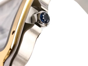Close-up of Santos Large Two Tone Yellow Gold watch with white dial, featuring a blue sapphire cabochon on the crown.